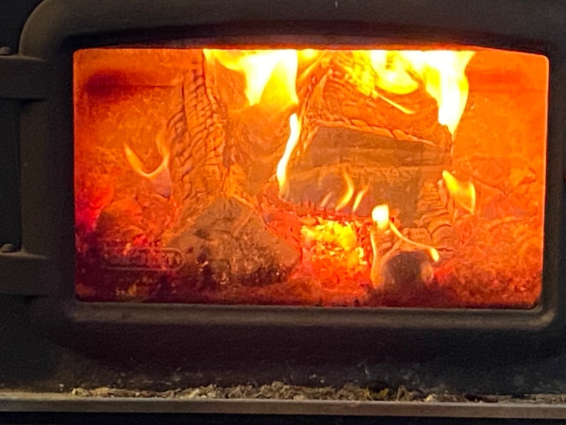 Pu&ograve; includere: Una vista ravvicinata di una stufa a legna con un fuoco incandescente all'interno. Le fiamme sono arancioni e gialle, e le  ceppi ardono vivacemente.