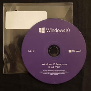 May include: A purple Windows 10 Enterprise Build 20H1 64-bit CD-ROM with the Microsoft logo, next to a clear plastic sleeve with a blank white label. The disc has the Windows 10 logo.