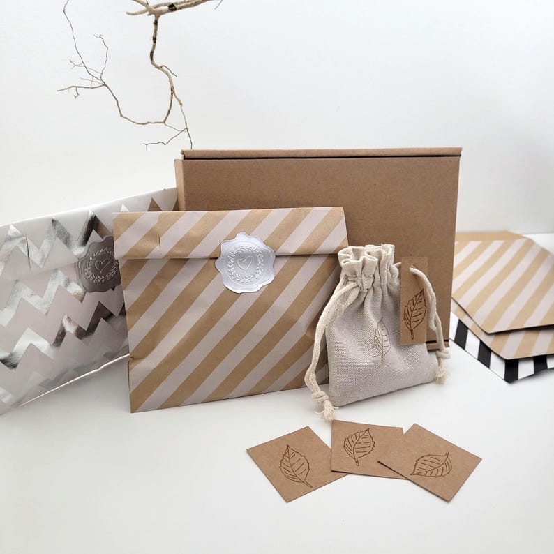 Eco-friendly packaging items. A brown paper bag with diagonal white stripes and a white wax seal, a small drawstring bag, and brown tags and cards with leaf illustrations. A brown cardboard box is in the background.