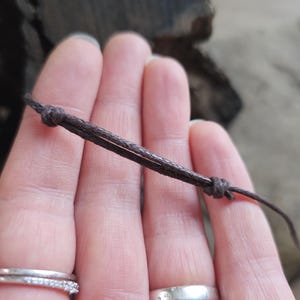 May include: A close-up of a brown cord with two knots. The cord is held in a person's hand.