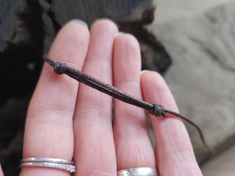 May include: A close-up of a brown cord with two knots. The cord is held in a person's hand.