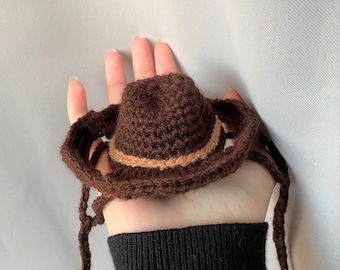 May include: A brown crocheted cowboy hat with a brown and tan band. The hat has long ties that can be tied under the chin.