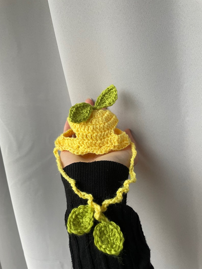 May include: A yellow crocheted lemon hat with green crocheted leaves. The hat has a long yellow crocheted strap with two green crocheted leaves at the end.