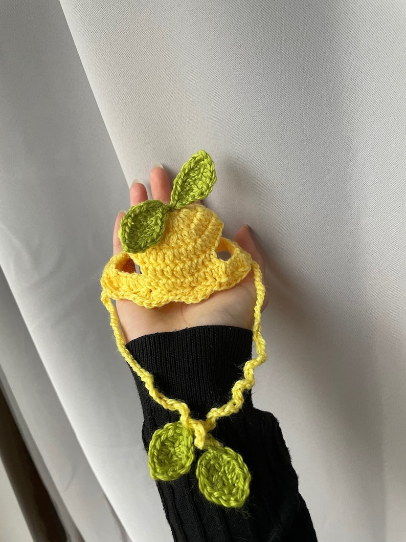 May include: A yellow crocheted lemon hat with green crocheted leaves. The hat has a long yellow crocheted string with two green crocheted leaves at the end.