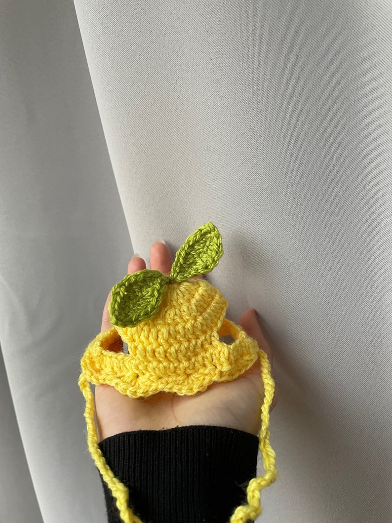 May include: A yellow crocheted lemon hat with green leaves. The hat has a strap that ties under the chin.
