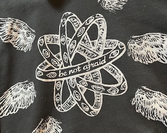 May include: Black hoodie with a white graphic print of a stylized atom with the text "be not afraid" and multiple white angel wings surrounding the atom.