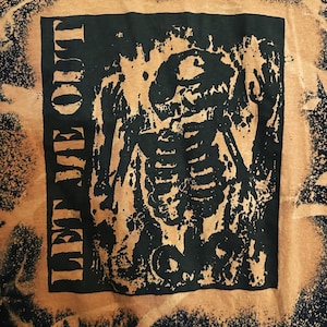 Könnte beinhalten: Ein schwarzes und braunes T-Shirt mit einem Design aus Bleichmittelspritzer. Das Design zeigt ein Schwarzweißbild eines Skeletts mit dem Text "Temple Of Out", der vertikal auf der linken Seite gedruckt ist.