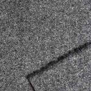 May include: Close-up of a gray tweed fabric with a textured surface. The fabric has a speckled appearance with small white and black flecks throughout. A folded edge reveals the fabric's thickness and weave.
