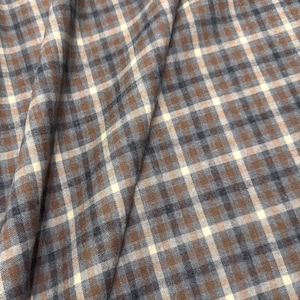 May include: Close-up of a fabric with a plaid pattern. The fabric features a repeating pattern of brown, off-white, and navy blue squares. The fabric is folded, creating shadows and depth, and is likely used for clothing or home decor.