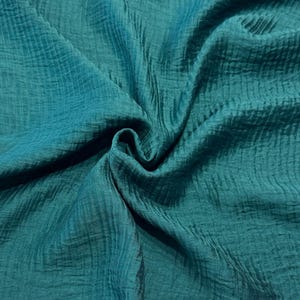 May include: Close-up of teal-colored fabric with a textured, crinkled appearance. The fabric is draped, creating folds and shadows that highlight its texture. The color is a deep, saturated teal, with variations in tone due to the folds.