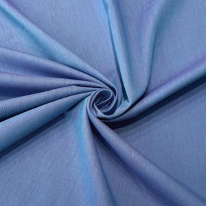 Könnte beinhalten: Nahaufnahme eines blauen Stoffes mit einem Wirbelmuster. Der Stoff hat einen subtilen Glanz und einen Farbverlauf, der von einem helleren Blau zu einem dunkleren Farbton übergeht. Die Textur erscheint glatt und weich.