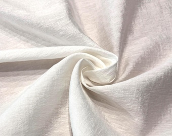 May include: A solid white fabric with a subtle, crinkled texture and a soft sheen. The material is gathered in the centre, creating deep, flowing folds and shadows that highlight the fine, horizontal grain of the textile surface throughout.