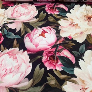 Pode incluir: Tecido floral com grandes pe&oacute;nias rosa e creme sobre um fundo escuro. As pe&oacute;nias t&ecirc;m p&eacute;talas detalhadas e s&atilde;o rodeadas por folhas verdes, criando um design bot&acirc;nico exuberante.
