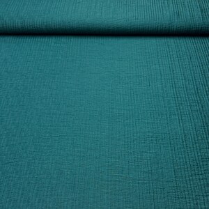 May include: Teal-colored fabric with a textured, crinkled appearance. The material is folded over at the top, revealing the layered texture. The fabric has a soft, matte finish and a subtle vertical pattern. Ideal for sewing projects.
