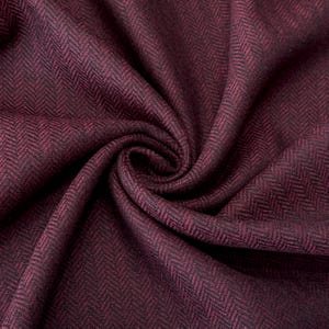 Gefalteter Fischgrät-Tweed in meliertem Weinrot und Schwarz, der die hochwertige Schurwollqualität und die modische Interpretation des klassischen Musters präsentiert. Der Wollstoff ist wärmend und robust, dabei wollig weich und angenehm im Griff.