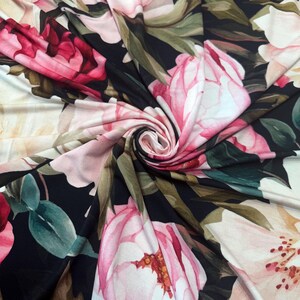 Pode incluir: Tecido floral com grandes flores rosa e vermelhas, folhas verdes e fundo preto. O tecido &eacute; rodopiado, mostrando o padr&atilde;o repetitivo e as varia&ccedil;&otilde;es de cor do design.