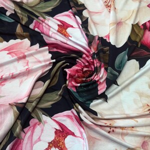 Pode incluir: Close-up de um tecido com um padr&atilde;o floral. O design apresenta grandes flores em estilo aquarela em tons de rosa, creme e vermelho sobre um fundo escuro. O tecido &eacute; drapeado, mostrando a textura e o fluxo do material.