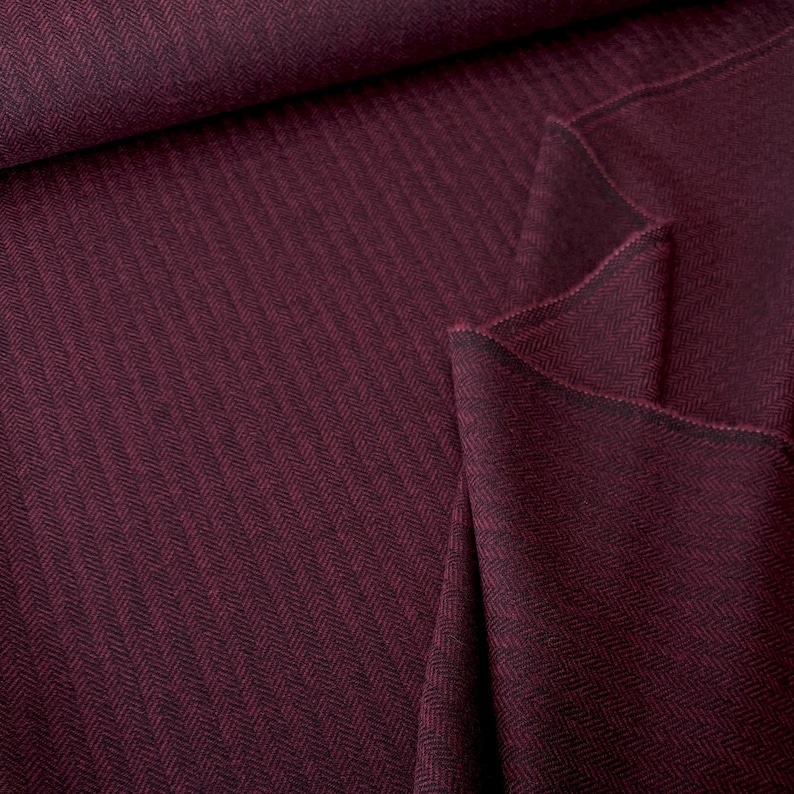 Gesamtansicht eines wunderschönen Fischgrät-Tweeds in Weinrot und Schwarz, in weiche Falten gelegt. Dieser hochwertige Schurwollstoff ist beidseitig verwendbar und eignet sich perfekt für warme Blazer, Jacken, Mäntel, Capes, Ponchos, Kostüme, Westen.