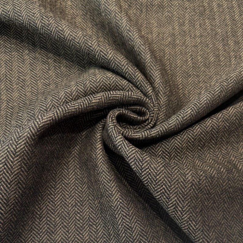 Op de afbeelding: Een bruine en donkergrijze stof met een klassiek visgraatpatroon. Het materiaal wordt getoond met zachte plooien en draperingen, wat de ingewikkelde V-vormige weefstructuur over het gehele oppervlak van het textielmateriaal benadrukt.