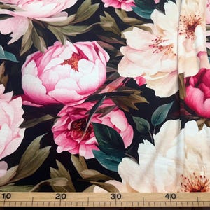 Pode incluir: Tecido floral com grandes pe&oacute;nias rosa e brancas sobre um fundo escuro. O tecido apresenta folhas verdes e uma r&eacute;gua na parte inferior, com medidas em cent&iacute;metros.