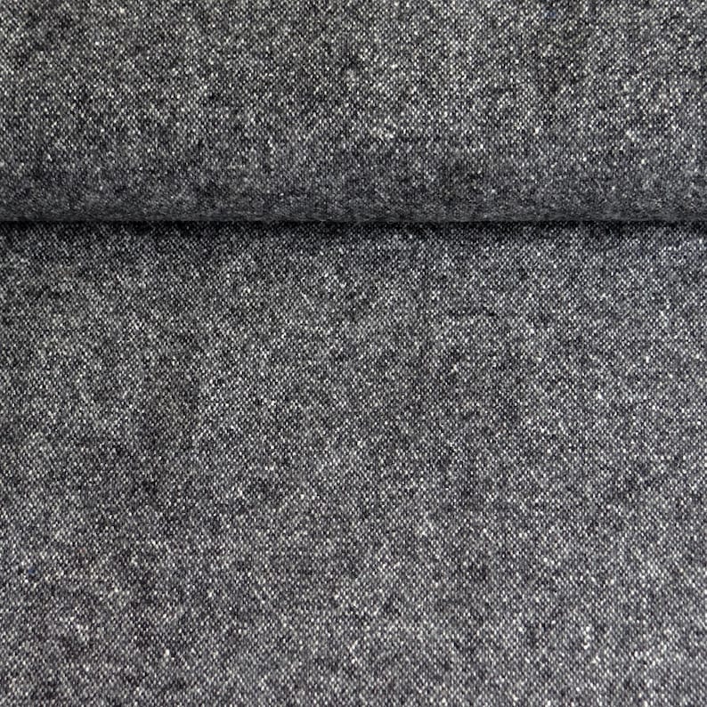 May include: Close-up of a textured, dark gray fabric with a subtle speckled pattern. The material appears to be folded over, revealing a layered effect. The fabric has a woven appearance, suggesting a durable textile.