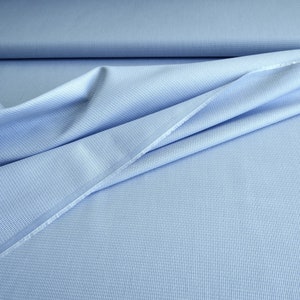 May include: Light blue fabric with a subtle textured pattern. The fabric is draped, showing folds and creases. The material appears to be a woven textile, possibly cotton or a blend, suitable for apparel or home decor projects.