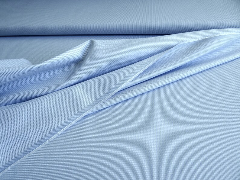 May include: Light blue fabric with a subtle textured pattern. The fabric is draped, showing folds and creases. The material appears to be a woven textile, possibly cotton or a blend, suitable for apparel or home decor projects.
