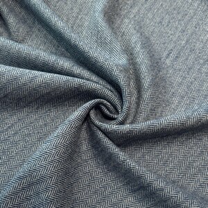 Gefalteter Fischgrät-Tweed in meliertem Blau und Hellgrau, der die hochwertige Schurwollqualität und die moderne Interpretation des klassischen Musters präsentiert. Der Wollstoff ist wärmend und robust, dabei wollig weich und angenehm im Griff.