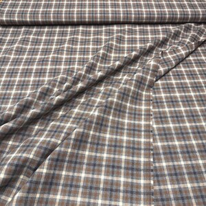 May include: Close-up of a fabric with a brown, white, and navy blue plaid pattern. The fabric is folded and draped, showing the texture and design. The plaid pattern is a classic design.