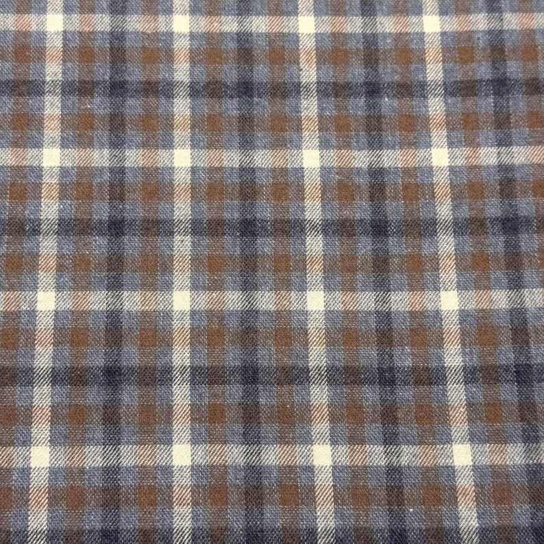 May include: Close-up of a fabric with a plaid pattern. The design features a grid of intersecting lines in brown, navy blue, and off-white. The fabric has a textured appearance, suggesting a woven material.
