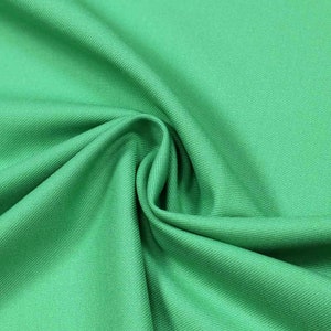 Könnte beinhalten: Nahaufnahme eines leuchtend grünen Stoffes mit einer dezenten Rippenstruktur. Das Material ist gefaltet, wodurch weiche Schatten entstehen und der Glanz des Stoffes hervorgehoben wird. Die leuchtende Farbe deutet auf einen Textilstoff für Kleidung oder Heimdekoration hin.