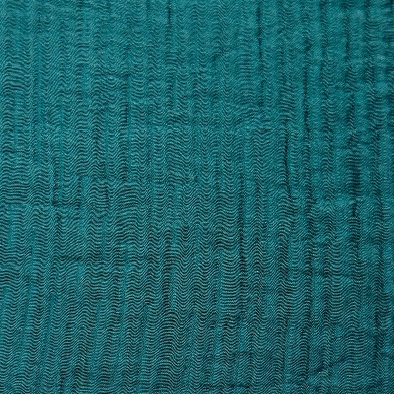 May include: Close-up of a teal-colored fabric with a textured, crinkled appearance. The fabric has a soft, flowing drape, with vertical and horizontal lines creating a subtle grid pattern. The color is a deep, saturated teal.