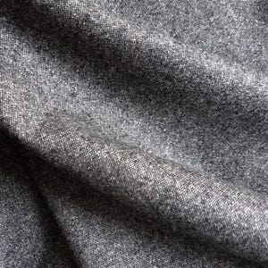 May include: Close-up of a textured gray fabric with subtle variations in tone. The material appears to be woven, with visible threads creating a slightly rough surface. The fabric is draped, showing folds and shadows.