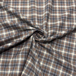 May include: Close-up of a fabric with a plaid pattern. The fabric features a repeating pattern of brown, white, and navy blue squares. The fabric is folded and draped, showing the texture and flow of the material.