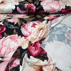 Pode incluir: Tecido floral com grandes pe&oacute;nias em tons de rosa, creme e vermelho sobre um fundo escuro. Folhas verdes s&atilde;o intercaladas entre as flores. O tecido est&aacute; dobrado, mostrando o padr&atilde;o em ambos os lados.