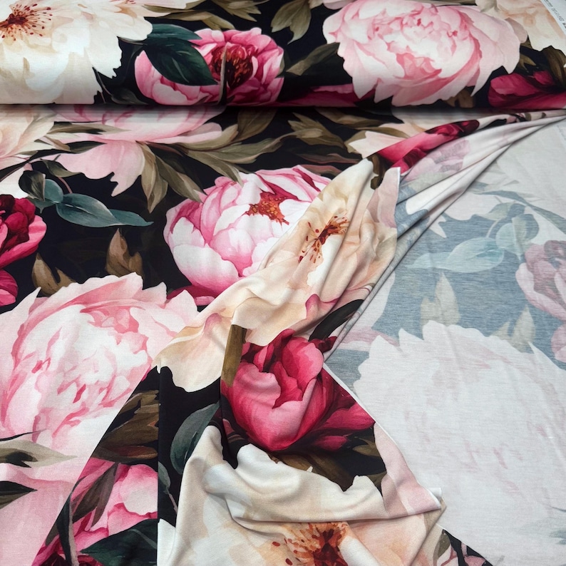 Pode incluir: Tecido floral com grandes pe&oacute;nias em tons de rosa, creme e vermelho sobre um fundo escuro. Folhas verdes s&atilde;o intercaladas entre as flores. O tecido est&aacute; dobrado, mostrando o padr&atilde;o em ambos os lados.