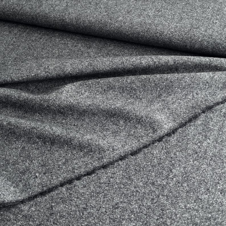 May include: Close-up of a gray fabric with a textured surface. The fabric is folded and draped, creating shadows and highlighting the material's texture. The fabric appears to be a medium-weight material, suitable for various sewing projects.