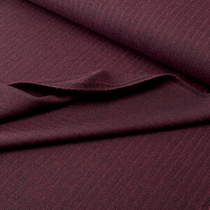 Gesamtansicht eines hochwertigen Fischgrät-Tweeds in Weinrot und Schwarz, in weiche Falten gelegt. Dieser toller Wollstoff aus Schurwolle ist beidseitig verwendbar und eignet sich perfekt für Blazer, Jacken, Mäntel, Capes, Ponchos, Kostüme, Westen.