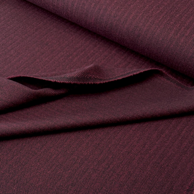 Gesamtansicht eines hochwertigen Fischgrät-Tweeds in Weinrot und Schwarz, in weiche Falten gelegt. Dieser toller Wollstoff aus Schurwolle ist beidseitig verwendbar und eignet sich perfekt für Blazer, Jacken, Mäntel, Capes, Ponchos, Kostüme, Westen.