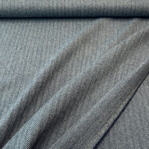 Gesamtansicht eines hochwertigen Fischgrät-Tweeds in Blau und Hellgrau, in weiche Falten gelegt. Dieser toller Wollstoff aus Schurwolle ist beidseitig verwendbar und eignet sich perfekt für Blazer, Jacken, Mäntel, Capes, Ponchos, Kostüme, Westen.