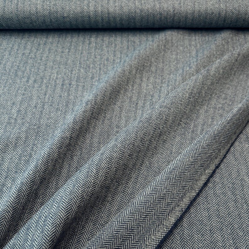 Gesamtansicht eines hochwertigen Fischgrät-Tweeds in Blau und Hellgrau, in weiche Falten gelegt. Dieser toller Wollstoff aus Schurwolle ist beidseitig verwendbar und eignet sich perfekt für Blazer, Jacken, Mäntel, Capes, Ponchos, Kostüme, Westen.