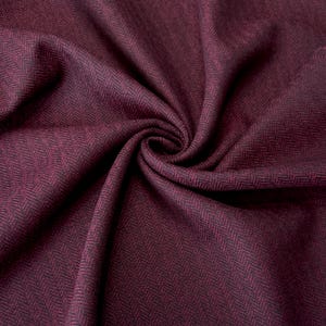 Detailaufnahme eines gefalteten Fischgrät-Tweeds in Weinrot und Schwarz. Die weiche Beschaffenheit und die exklusive Schurwolle machen den Stoff ideal für stilvolle Bekleidungsstücke wie Mäntel, Capes und winterwarme Westen.