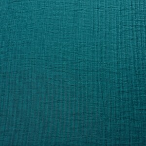 May include: Close-up of a teal fabric with a textured, crinkled appearance. The fabric has a vertical ribbed pattern, creating a subtle striped effect. The color is a deep, saturated teal, with variations in tone due to the texture.