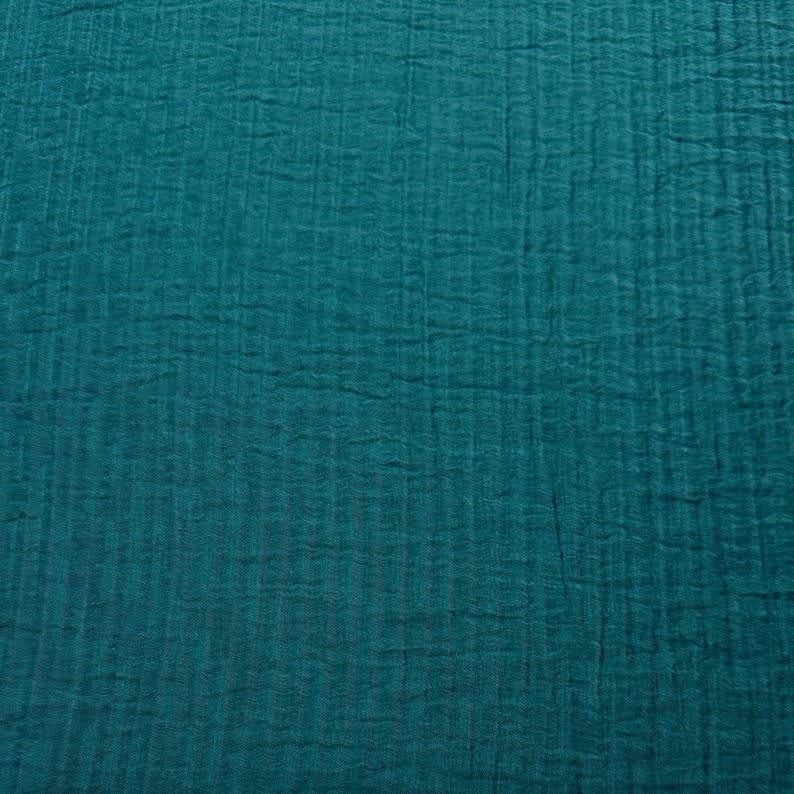 May include: Close-up of a teal fabric with a textured, crinkled appearance. The fabric has a vertical ribbed pattern, creating a subtle striped effect. The color is a deep, saturated teal, with variations in tone due to the texture.