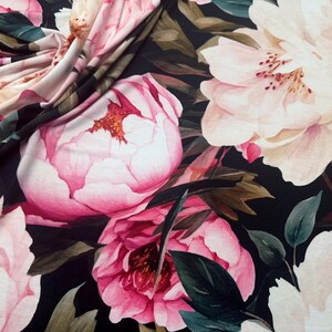 Pode incluir: Close-up de tecido com um padr&atilde;o floral. Grandes pe&oacute;nias cor-de-rosa e folhas verde-escuras num fundo preto. O tecido est&aacute; dobrado, mostrando a textura e profundidade do design.