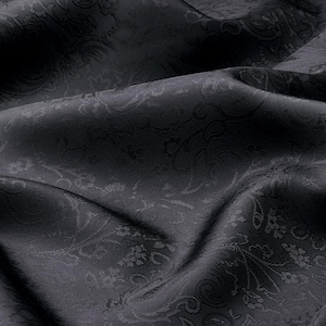 May include: A black fabric featuring a tonal jacquard weave with an intricate floral and paisley pattern. The material displays a subtle sheen and is captured in soft, flowing folds that highlight the depth and texture of the woven design.