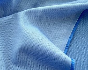 May include: Close-up of a light blue fabric with a textured, dotted pattern. The fabric is folded, showing the weave and the raw edge with a fringe. The color is a solid, pale blue.