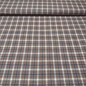 May include: Close-up of a fabric with a plaid pattern. The fabric features a grid of intersecting lines in brown, white, and navy blue. The fabric is folded over at the top, showing the texture and pattern. Suitable for apparel or home decor.