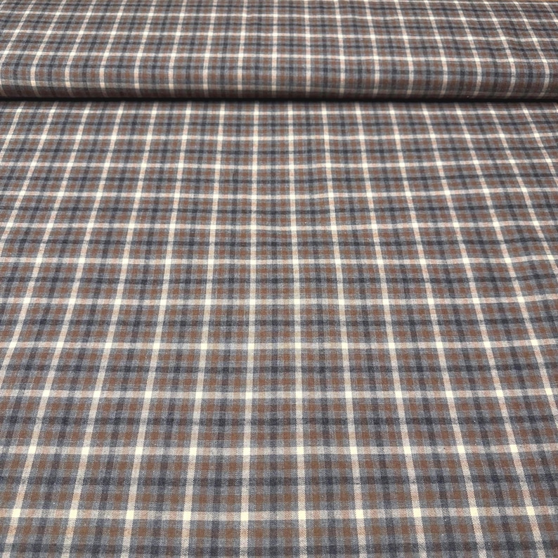May include: Close-up of a fabric with a plaid pattern. The fabric features a grid of intersecting lines in brown, white, and navy blue. The fabric is folded over at the top, showing the texture and pattern. Suitable for apparel or home decor.