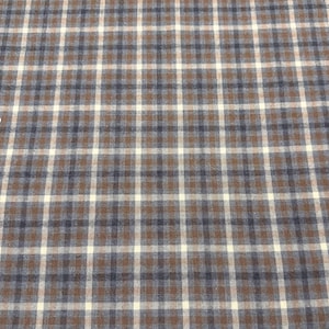 May include: A close-up of a fabric with a plaid pattern. The pattern features a grid of intersecting lines in brown, white, and navy blue. The fabric has a textured appearance.